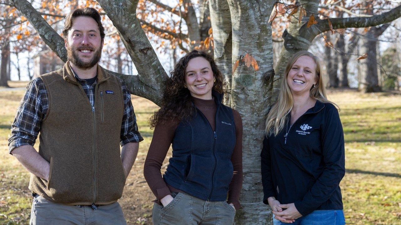 (From left) Eric Thompson, Jordan Thompson ’23, M.S. ’25, and Carrie Fearer in front of a beech tree near the Duck Pond on the Blacksburg campus. Photo by Max Esterhuizen for Virginia Tech.